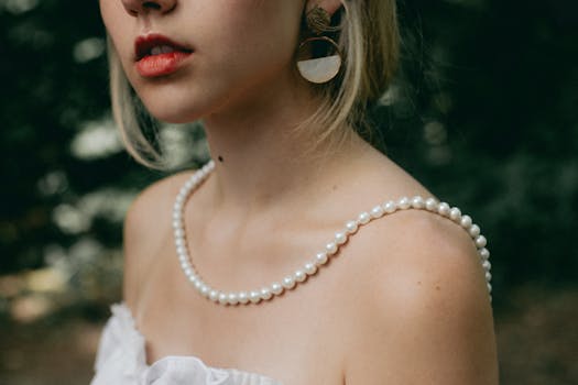 Elegant close-up portrait of a woman with pearl necklace and stylish earrings, wearing a white dress.