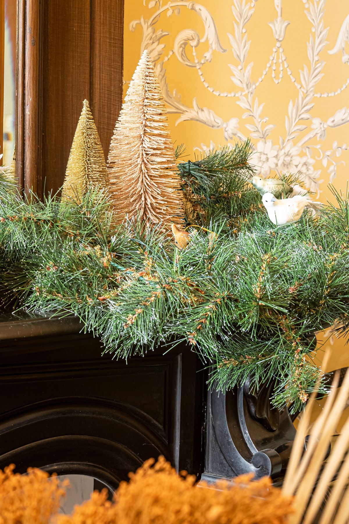 Cozy Christmas mantel lined with miniature decorative trees and greenery