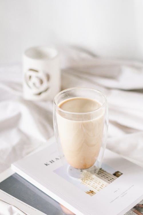 Free Double Wall Cup of Milky Coffee Standing on Book Laying by Bed Stock Photo