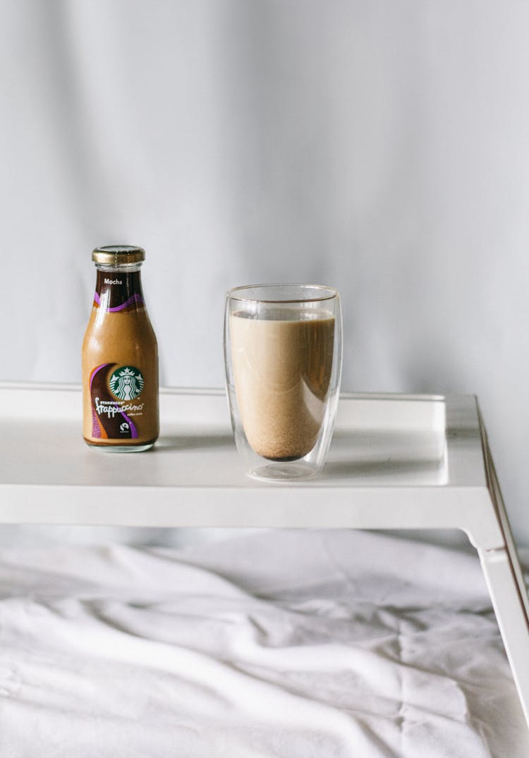 Glass Cup And Bottle Of Milky Frappuccino Standing On Bed Tray