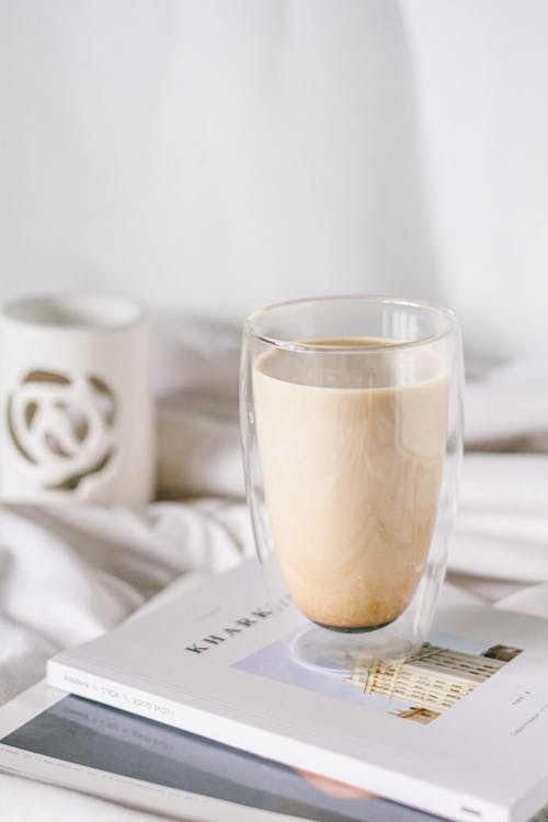 Free Coffee with Foamed Milk in Double Wall Glass Mug Standing by Bed Stock Photo