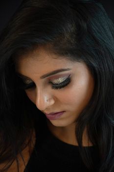 Close-up portrait of a woman with glittery eyeshadow, looking down thoughtfully.