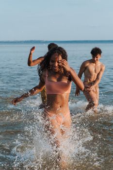 Group of teenagers having fun in the sea, splashing water during a sunny summer day.