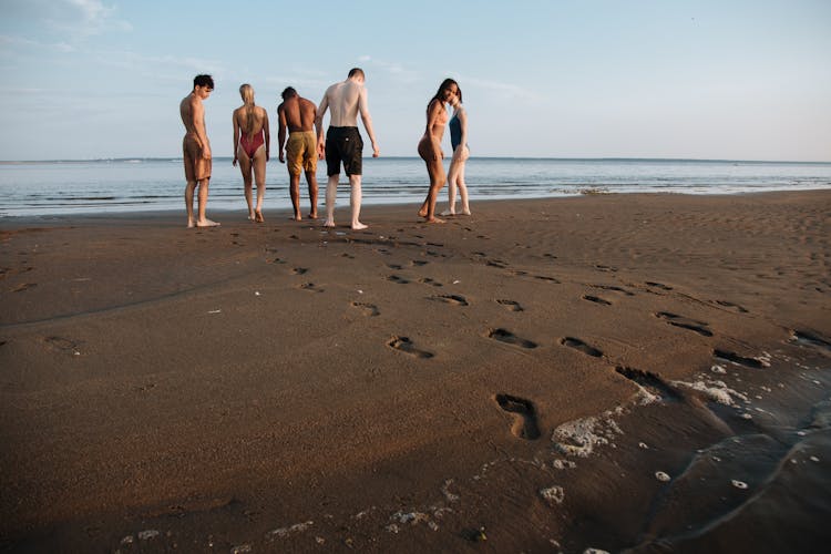 Diverse Group Of People In Swimwear Looking For Something In Sandy Beach