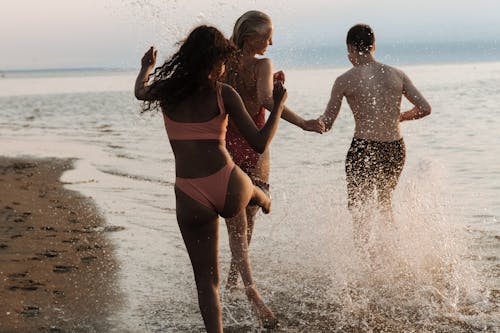 Free Teenagers Running Through Shallow Water on Beach Shore Stock Photo