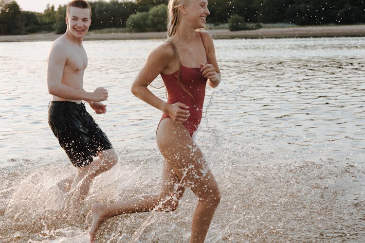 Boy And Girl In Swimwear Running Along Shore