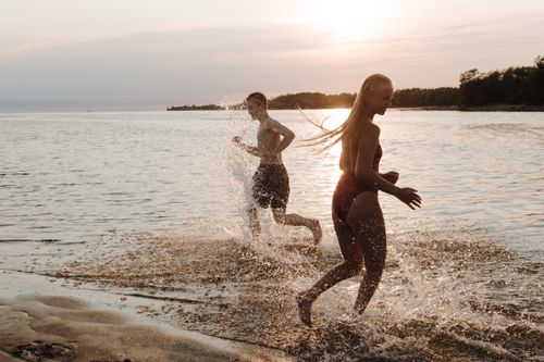 Free Two teenagers running on a beach at sunset, enjoying the summer seaside with splashes. Stock Photo