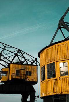 Two yellow industrial cranes stand prominently against a clear blue sky.