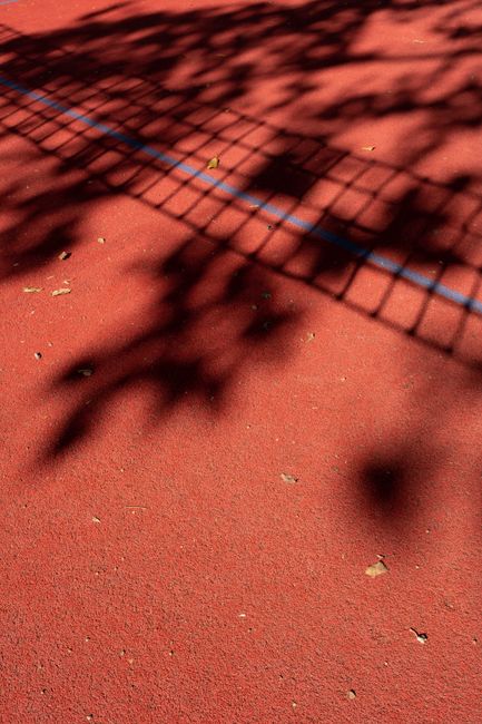Shadow of a fence on a vibrant red tennis court leaves a striking visual pattern.