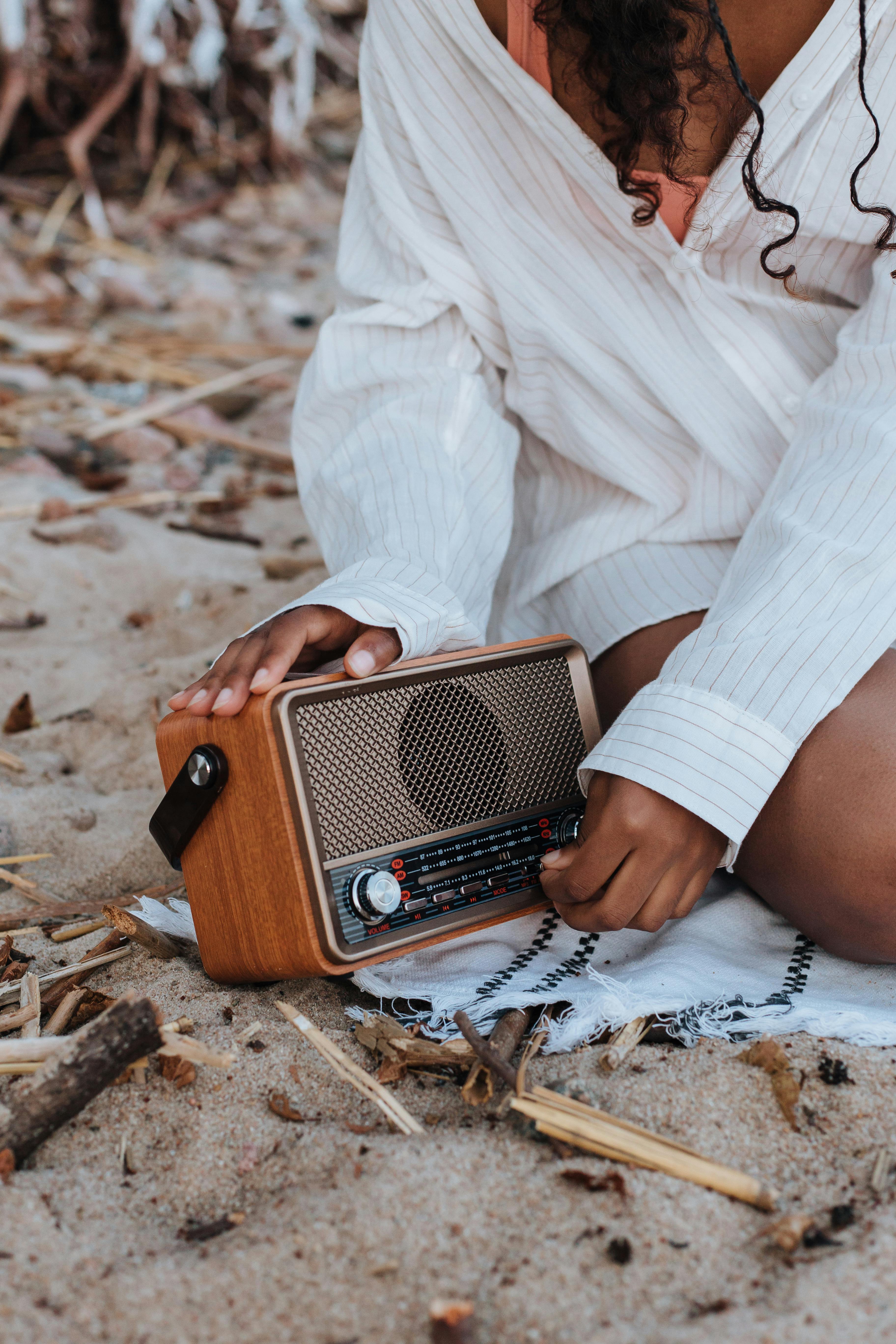 Young girl adjusts vintage radio on sandy beach, enjoying a summer day.