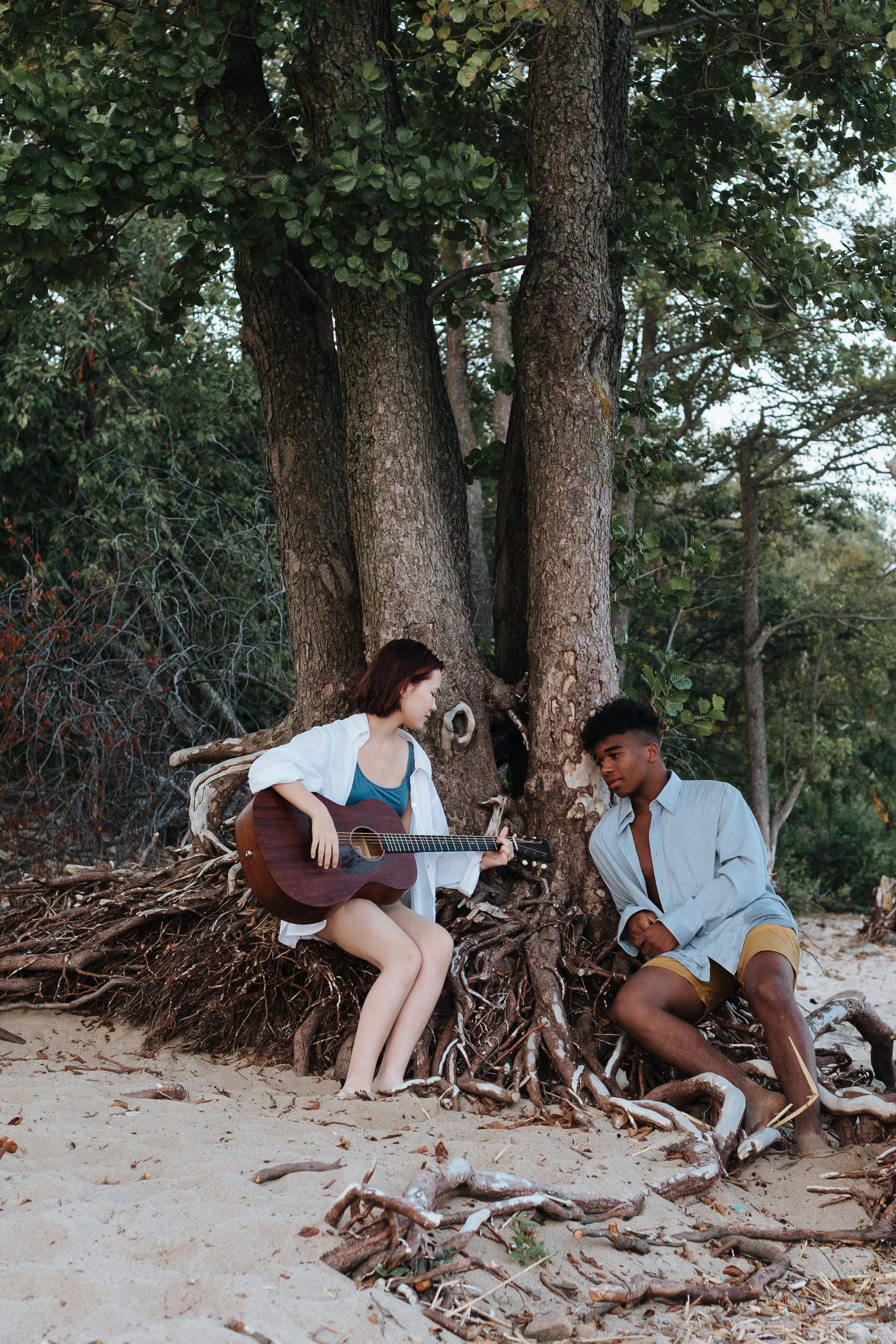 girl playing on the acoustic guitar and boy listening to it