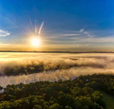 A breathtaking aerial view of a sunrise casting light over fog and trees in Wisconsin.