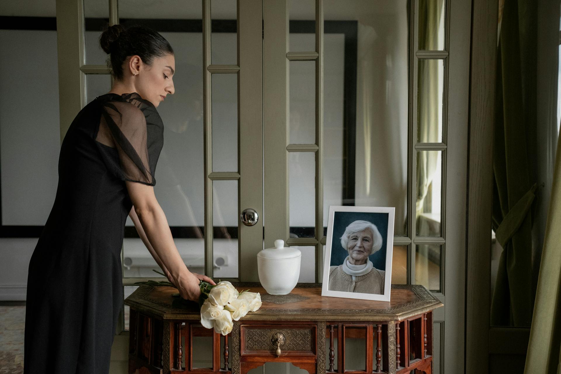 Mourner in Black Dress Standing by Table with Urn