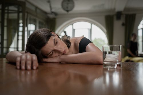Free A woman in a black dress rests her head on a table beside a glass of water, conveying sadness. Stock Photo