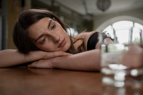Free Pensive woman resting her head on a wooden table with a glass of water nearby, indoors. Stock Photo