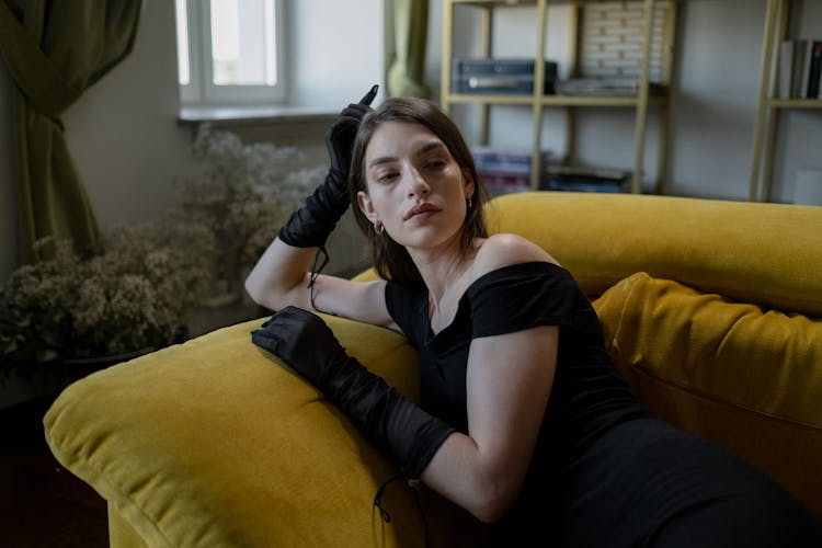 Woman In Black Dress Sitting On A Couch While Posing At The Camera