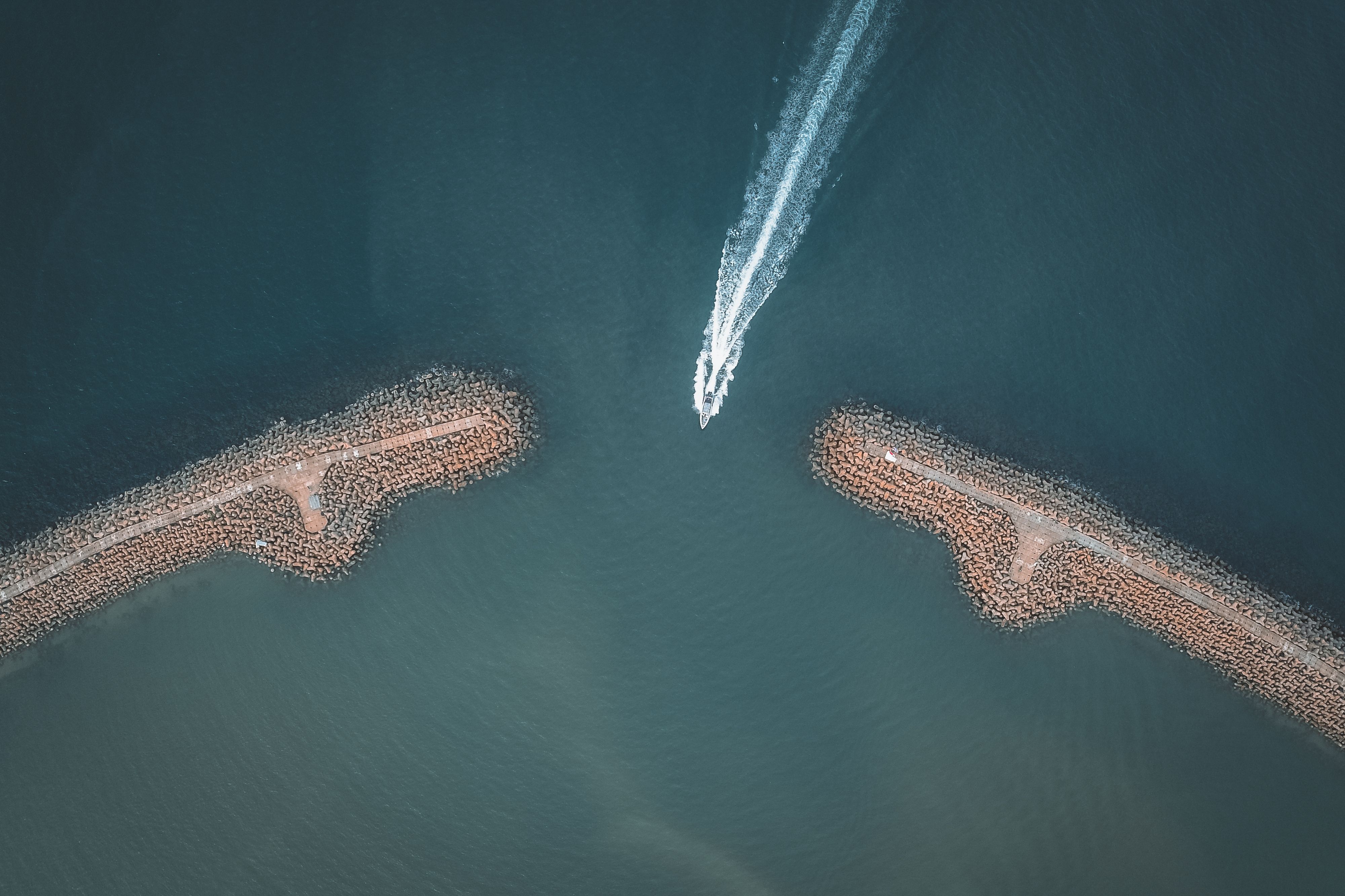 Drone shot capturing a speed boat maneuvering through a rocky ocean inlet.