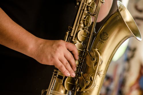 бесплатная Человек в черной рубашке играет на саксофоне латунного цвета Стоковое фото