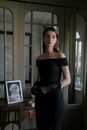 Woman in Black Off Shoulder Dress Standing Beside Glass Window