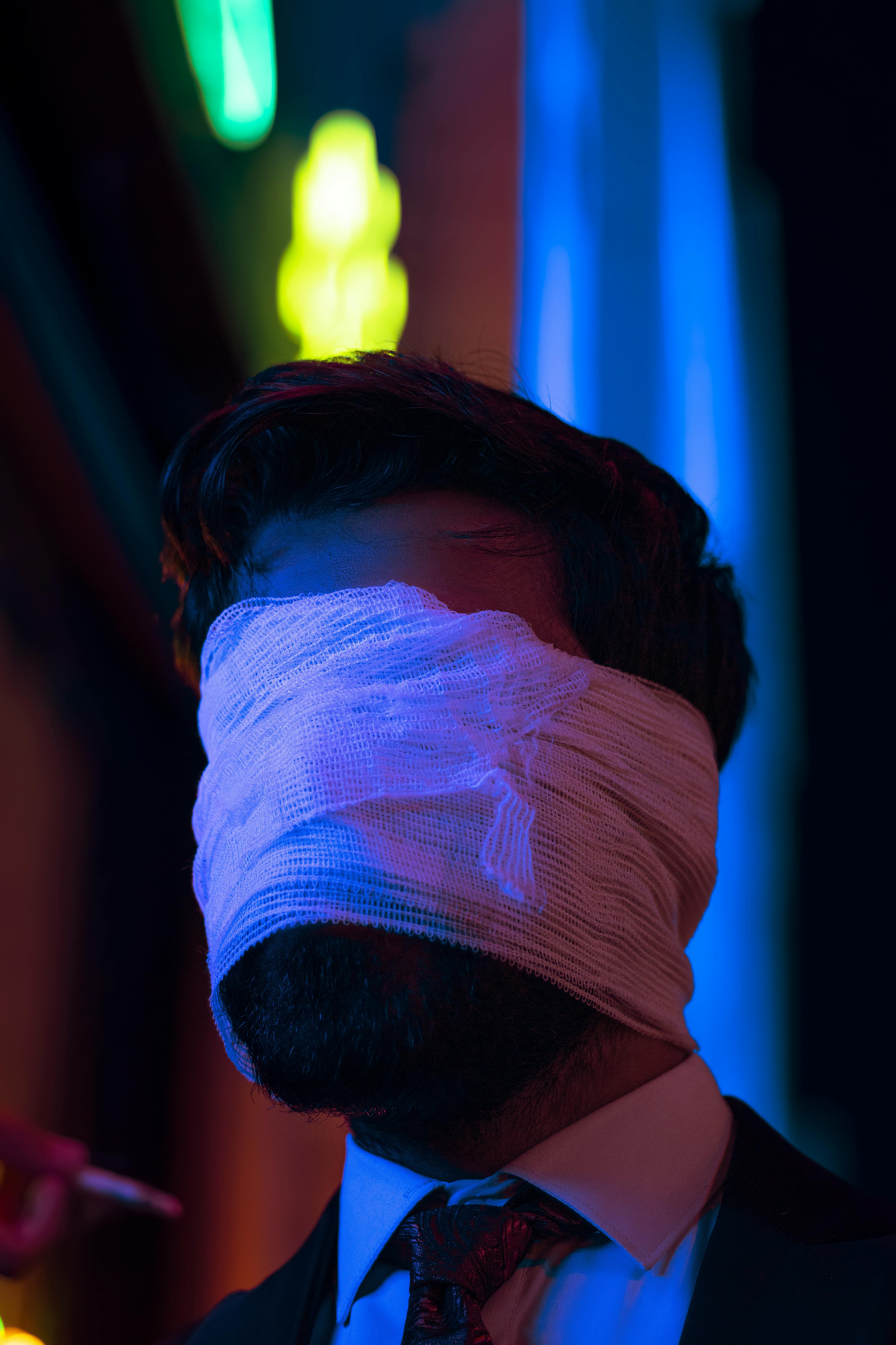 man with bandage on eyes with lights on background