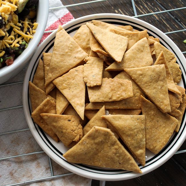 A bubbling baked corn dip in a square white baking dish, topped with melted pepper jack cheese, crumbled cotija, sliced green onions, and cilantro, with tortilla chips arranged around the edge.