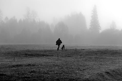 Grayscale Photo of a Person Running with a Dog on Grassland