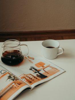 A stylish coffee setup with a cup and carafe alongside an open magazine, exuding relaxation.
