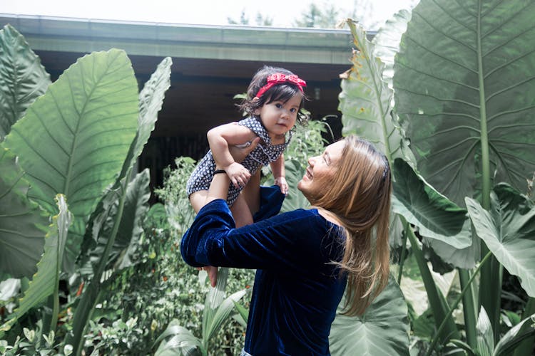 Woman In Blue Long Sleeves Lifting Up Baby 