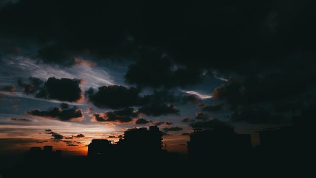 Silhouetted buildings against a vibrant evening sky with dramatic clouds.