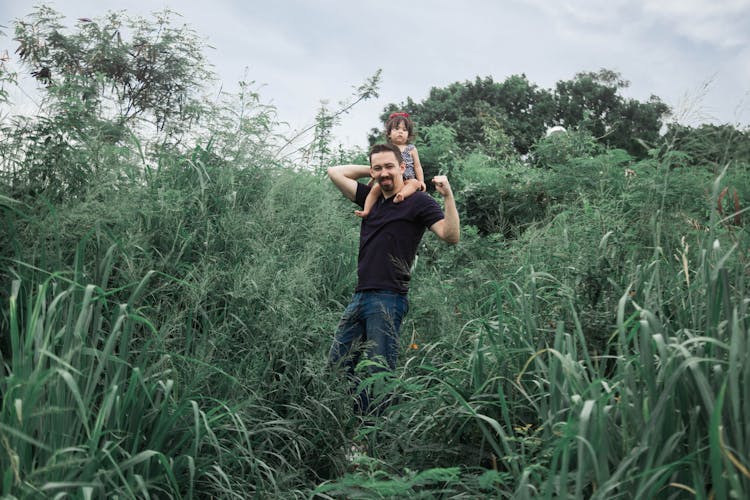 A Man Carrying A Baby On His Back While Standing On The Tall Grass