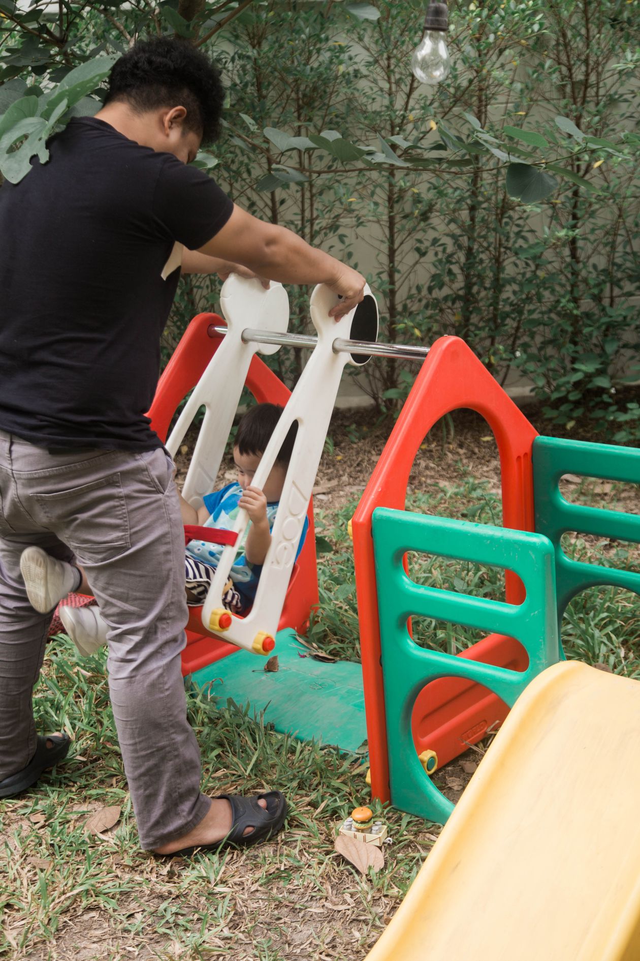 Parent pushing a toddler on an outdoor backyard swing, a gross motor outdoor toy