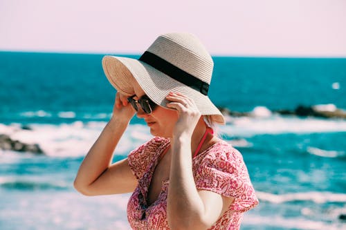 Free Selective Focus Photo of Woman Wears Beige Sun Hat Stand Behind Body of Water a Daytime Stock Photo