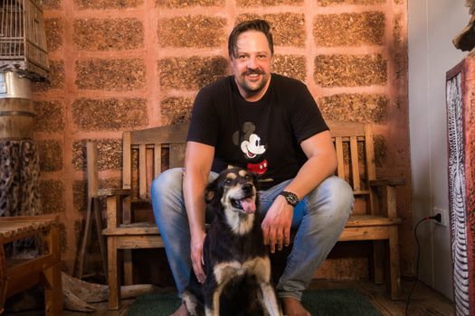 Man and dog share a joyful moment on wooden bench indoors.