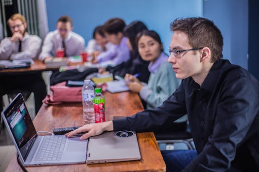 A group of students working together in a classroom with laptops and documents.