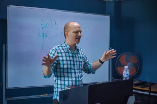 Caucasian man passionately explains concepts on a whiteboard in a classroom setting.