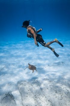 A scuba diver swimming alongside a sea turtle in the clear blue ocean depths.