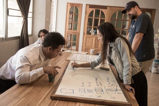 Team members engaged in discussion around a blueprint on a whiteboard.