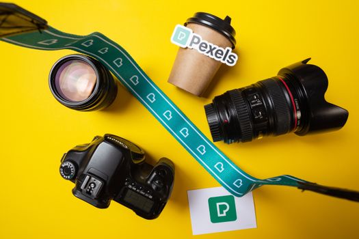 Flat lay of camera, lens, and coffee cup on a vibrant yellow background.