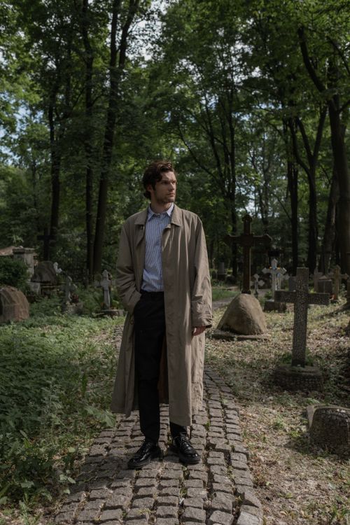 Free A man in a trench coat walks along a path in a serene forest cemetery. Stock Photo