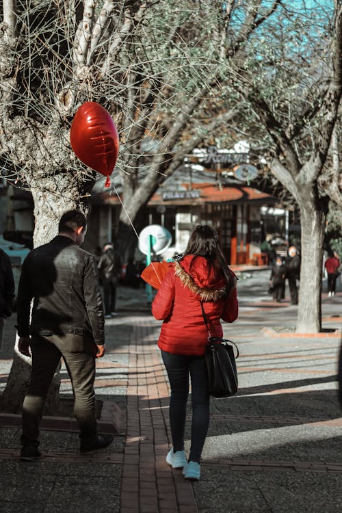 Back View of a Woman Walking while Holding a Heart-Shaped Balloon