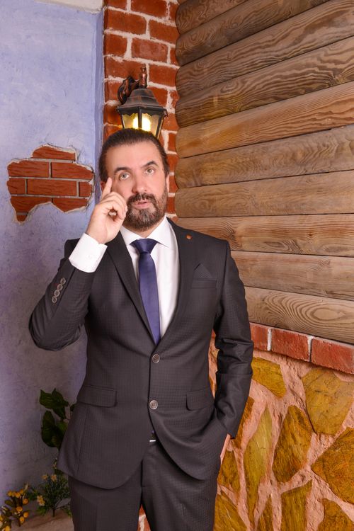 Free Bearded man in a formal suit indoors with brick and wood elements, posing near a lamp. Stock Photo