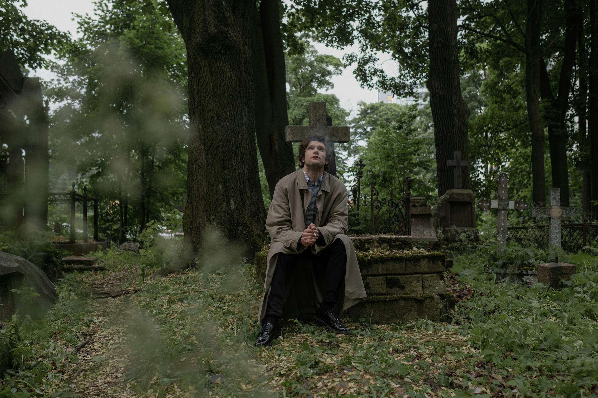 A Man Smoking a Cigarette while Sitting on a Grave