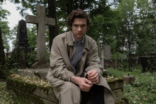 A Man in a Trench Coat Sitting on a Grave