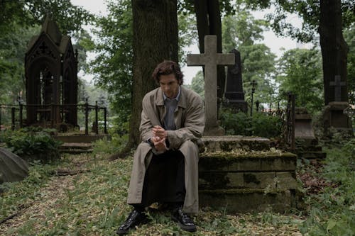 Free A Man in a Trench Coat Sitting on a Grave Stock Photo