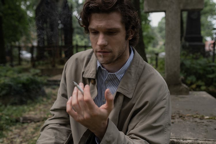 A Man Smoking A Cigarette At A Cemetery