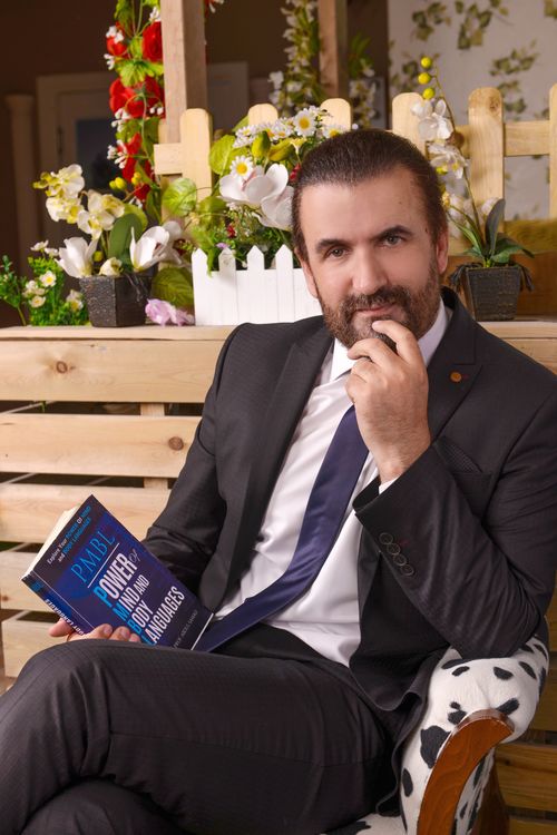 Free Man in black suit holding a book while sitting indoors with decorative flowers. Stock Photo