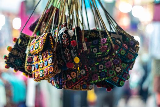 Vibrant handmade embroidered bags with buttons and strings, hung in a bustling market stall.