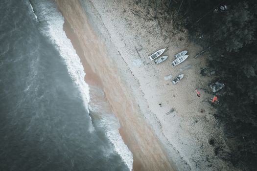 Drone shot capturing boats on a sandy beach with waves crashing ashore.