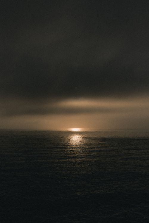 Free Serene sunset over the ocean with dark clouds and shimmering water reflection. Stock Photo
