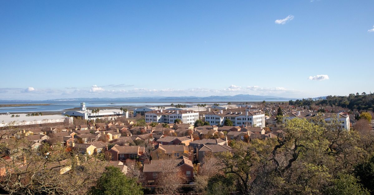Aerial view of suburban houses with tiled roofs under a clear blue sky.